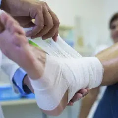 Lekarz bandażuje nogę pacjentki z obrzękiem limfatycznym, stosując kompresję dla ulgi.