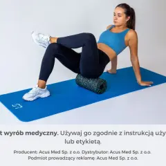 Kobieta na macie rehabilitacyjnej demonstruje, jak masować mięsień gruszkowaty za pomocą rollera.