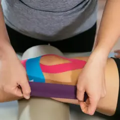 Fizjoterapeuta aplikuje kolorowe plastry na kolano, wykonując kinesio taping.