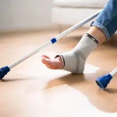 Osoba w opasce na kostce, z kulami, rozpoczyna chodzenie po artrodezie stawu skokowego.