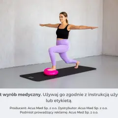 Kobieta wykonuje ćwiczenia równowagi na różowej poduszce sensorycznej, stojąc na macie.