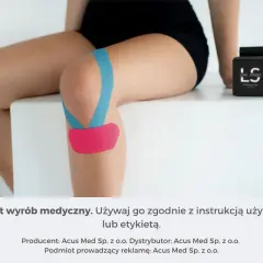 Kolano z niebieskim i różowym plastrem, zapewniającym stabilizację. Obok pudełko z taśmą.