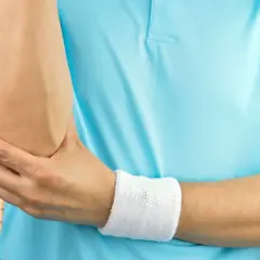 Mężczyzna w niebieskiej koszulce z opaską na nadgarstku, trzymający się za łokieć. Test na łokieć tenisisty.