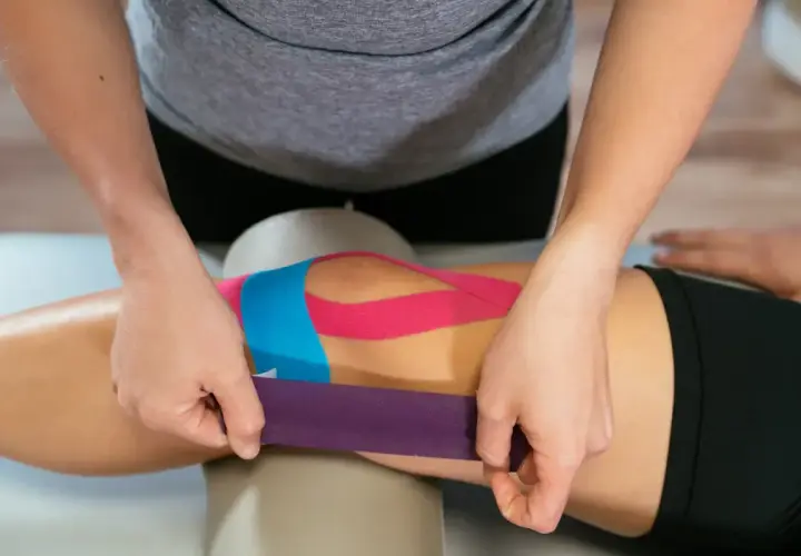 Fizjoterapeuta aplikuje kolorowe plastry na kolano, wykonując kinesio taping.