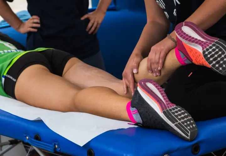 Masażysta wykonuje drenaż limfatyczny nogi sportowca, przygotowując ją do dalszych wysiłków.