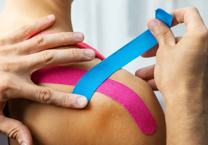 Kinesiotaping: niebieska i różowa taśma na ramieniu. Kolory w kinesiotapingu mogą mieć znaczenie terapeutyczne.