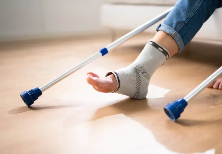 Osoba w opasce na kostce, z kulami, rozpoczyna chodzenie po artrodezie stawu skokowego.