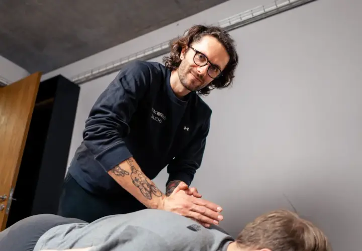 Fizjoterapeuta z tatuażami na ramieniu wykonuje masaż. Zastanawiasz się, ile trwa wizyta u fizjoterapeuty?