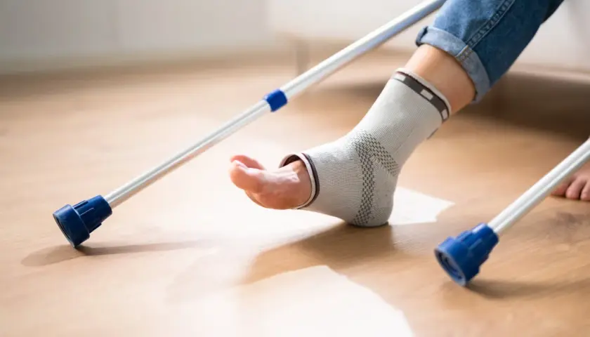 Osoba w opasce na kostce, z kulami, rozpoczyna chodzenie po artrodezie stawu skokowego.