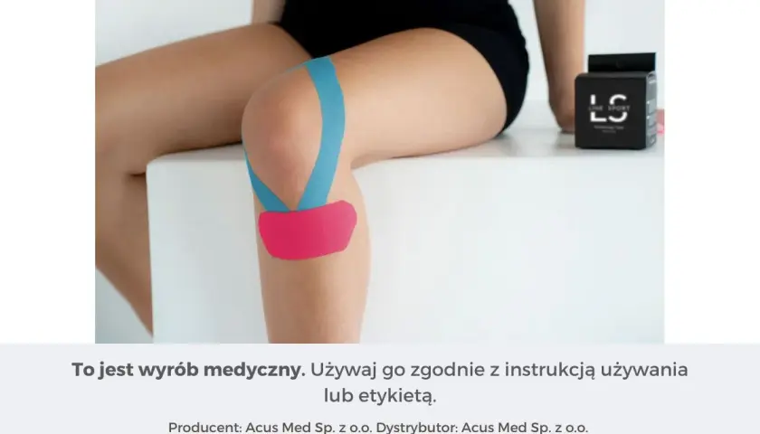 Kolano z niebieskim i różowym plastrem, zapewniającym stabilizację. Obok pudełko z taśmą.