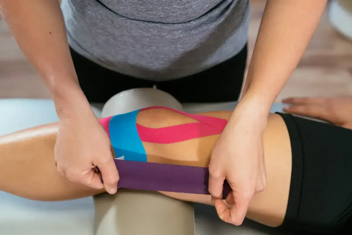 Fizjoterapeuta aplikuje kolorowe plastry na kolano, wykonując kinesio taping.