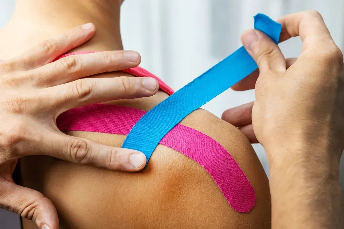 Kinesiotaping: niebieska i różowa taśma na ramieniu. Kolory w kinesiotapingu mogą mieć znaczenie terapeutyczne.