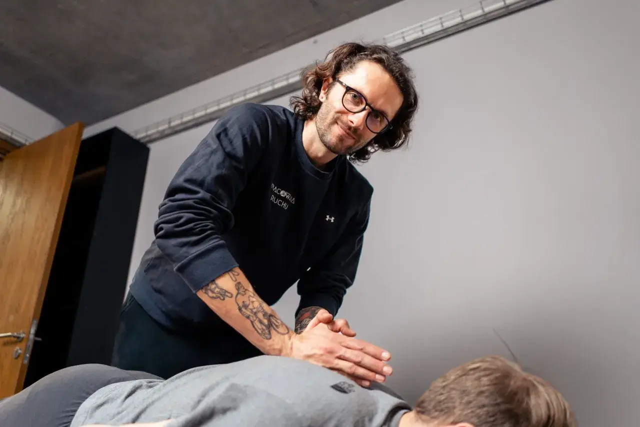 Fizjoterapeuta z tatuażami na ramieniu wykonuje masaż. Zastanawiasz się, ile trwa wizyta u fizjoterapeuty?