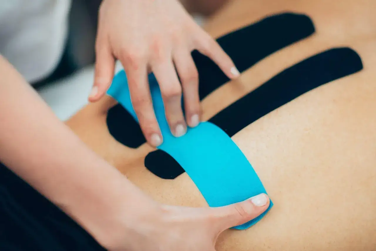 Terapeuta aplikuje niebieski plaster na plecy pacjenta. Ważne, by znać kinesiotaping przeciwwskazania.