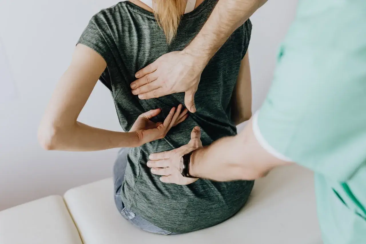 Fizjoterapeuta bada plecy pacjentki, szukając przyczyn bólu. Dowiedz się, jakie zabiegi na rwę kulszową mogą pomóc.